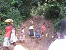 森の谷間にある浅井戸で汲んだ水を持ち帰る子ども達